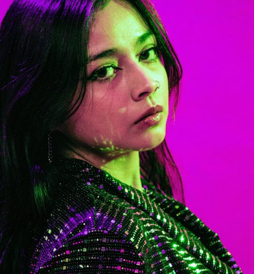 Portrait of a young adult with vibrant purple and green lighting, creating a modern and artistic vibe.